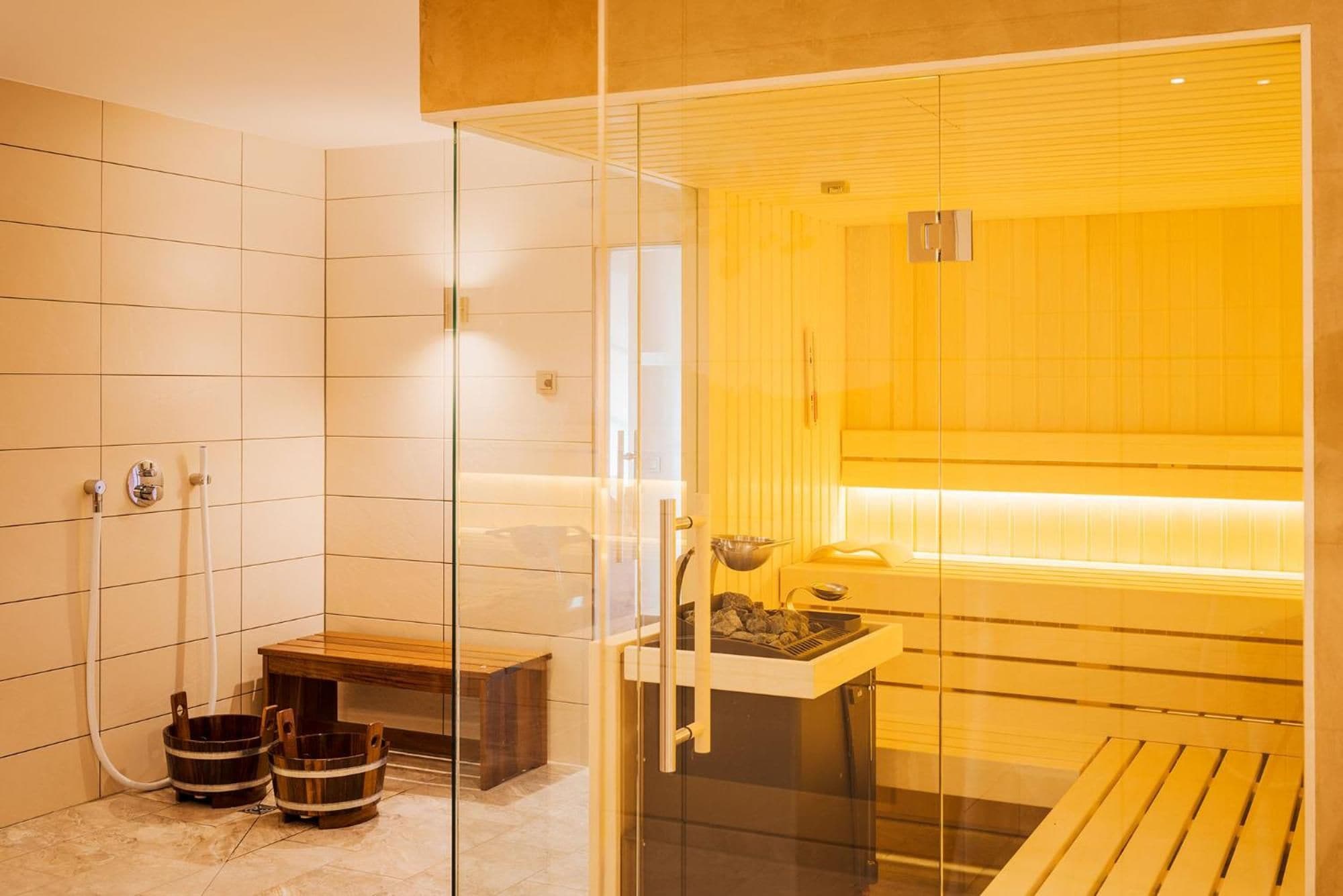 Un sauna con separador de vidrio, bancos de madera y un banco con un tazón.