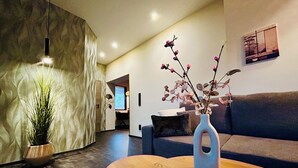 A modern living room with a sofa, a coffee table, a vase with branches, a potted plant, and a wall-mounted picture. - Hotel Reindahls (Altlandsberg)