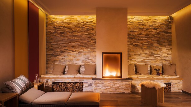 A cozy lounge area with a stone wall, a fireplace, and comfortable seating. - Hotel Reindahls (Altlandsberg)