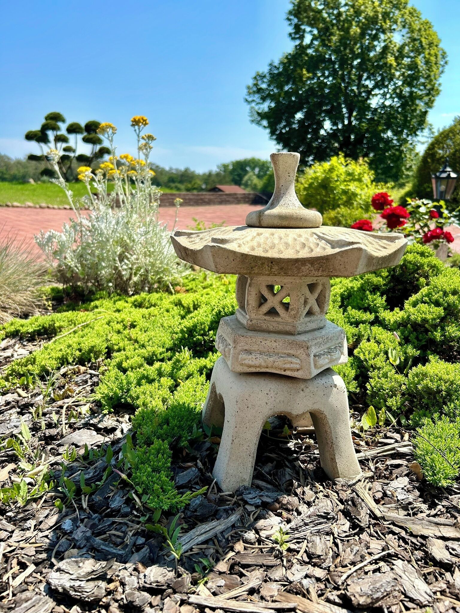 A stone lantern in a garden with green shrubs and mulch.