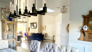 A dining area with a long table, multiple chairs, a chandelier, and a television mounted on the wall. - Elegant West Side Mountain Retreat (Tucson)