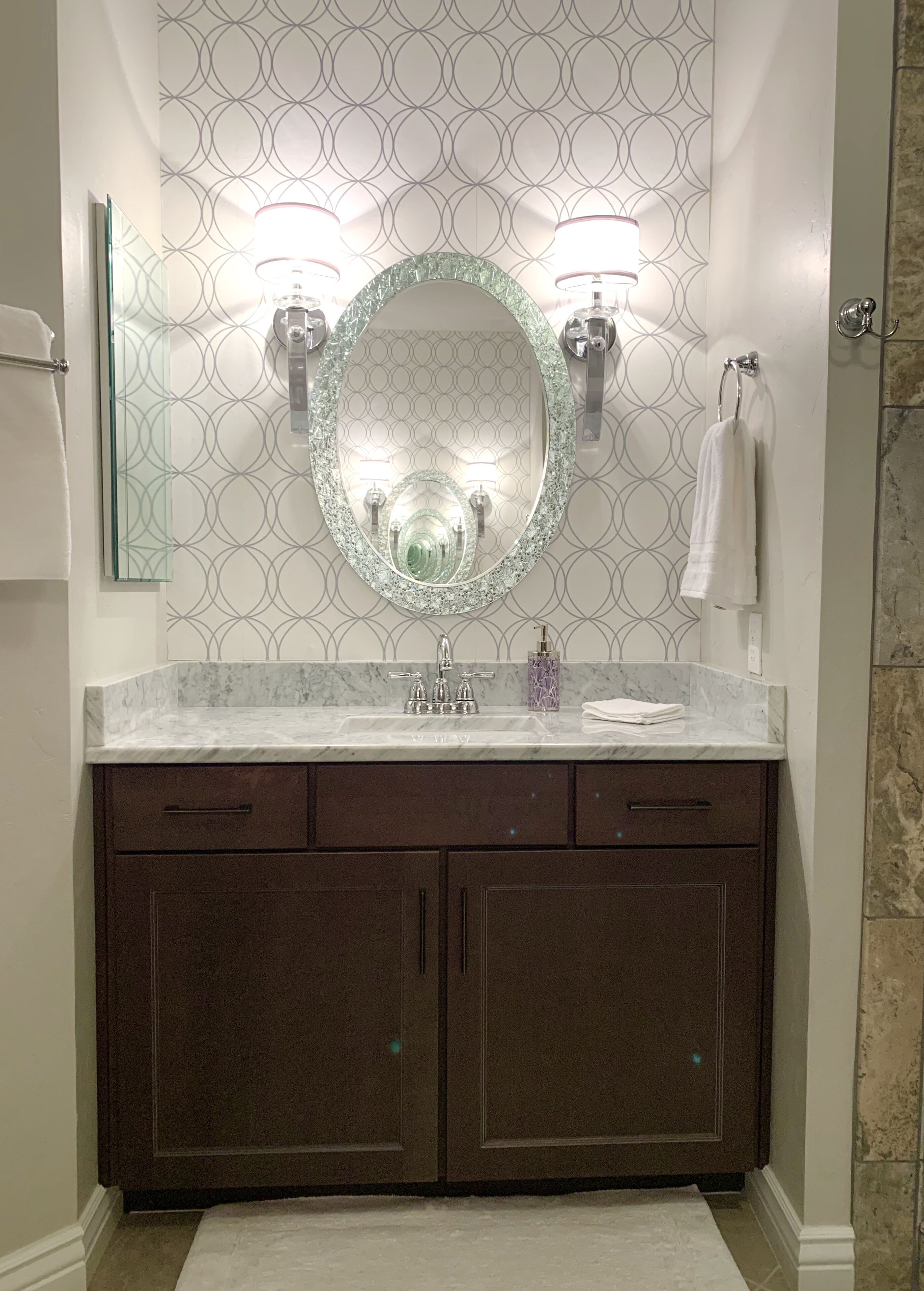 A bathroom with a marble vanity, a large mirror, two wall-mounted lights, and a towel rack.