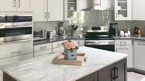 A modern kitchen with white cabinets, stainless steel appliances, and a marble island. - Elegant West Side Mountain Retreat (Tucson)