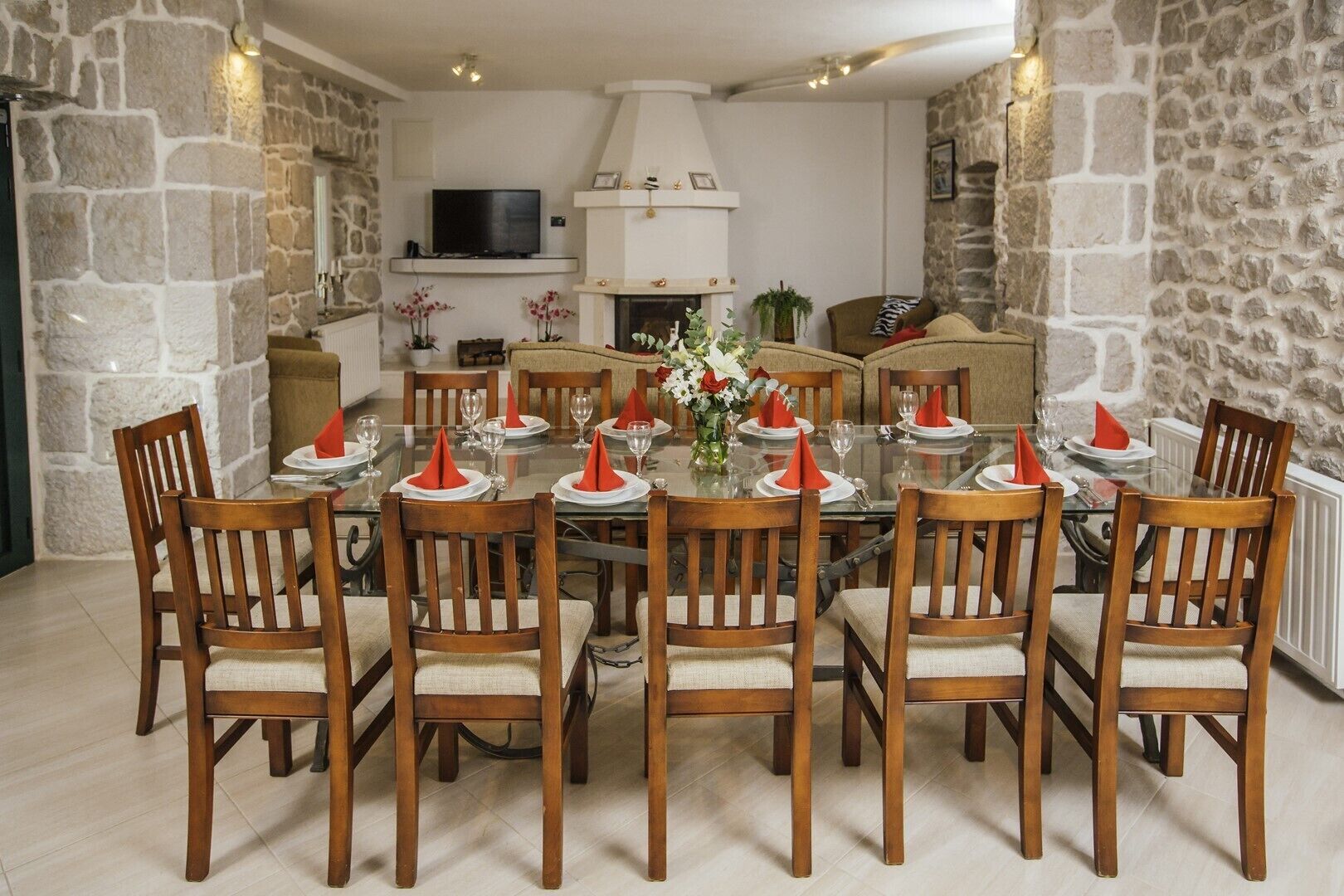 A dining area with a round glass table set for eight, surrounded by wooden chairs with cushioned seats.