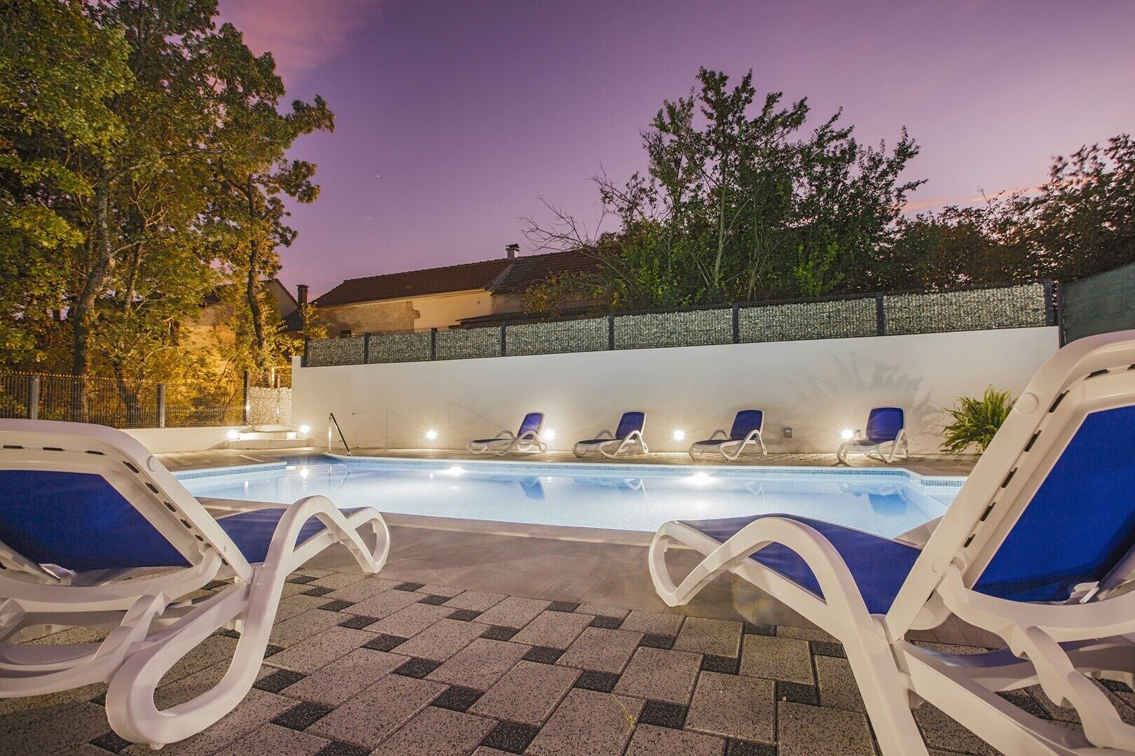 A swimming pool with lounge chairs and a stone wall in the background.