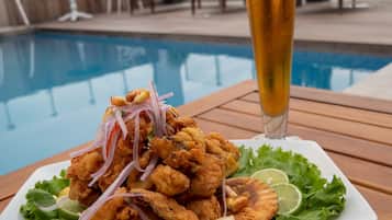 Plat de menjar fregit amb un got de cervesa sobre una taula de fusta al costat d'una piscina.