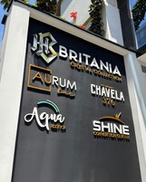 Un letrero con varios nombres de negocios, incluyendo 'Britania Crystal Collection', 'Aurum Bar', 'Chavela 376', 'Aqua Rooftop' y 'Shine Convention Center'.