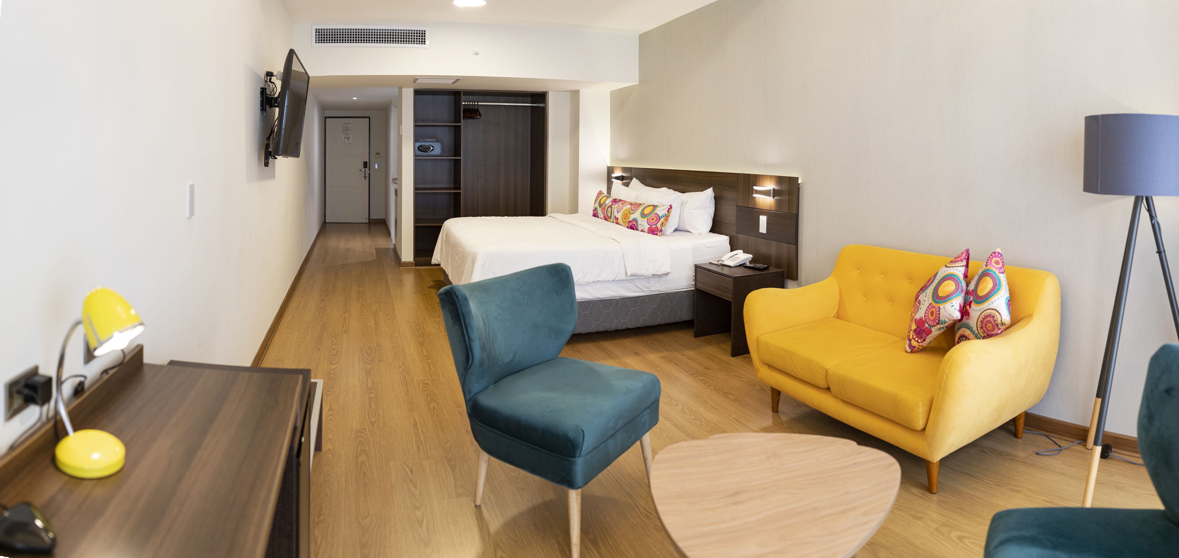 A hotel room with a bed, a desk, a chair, a sofa, and a floor lamp.