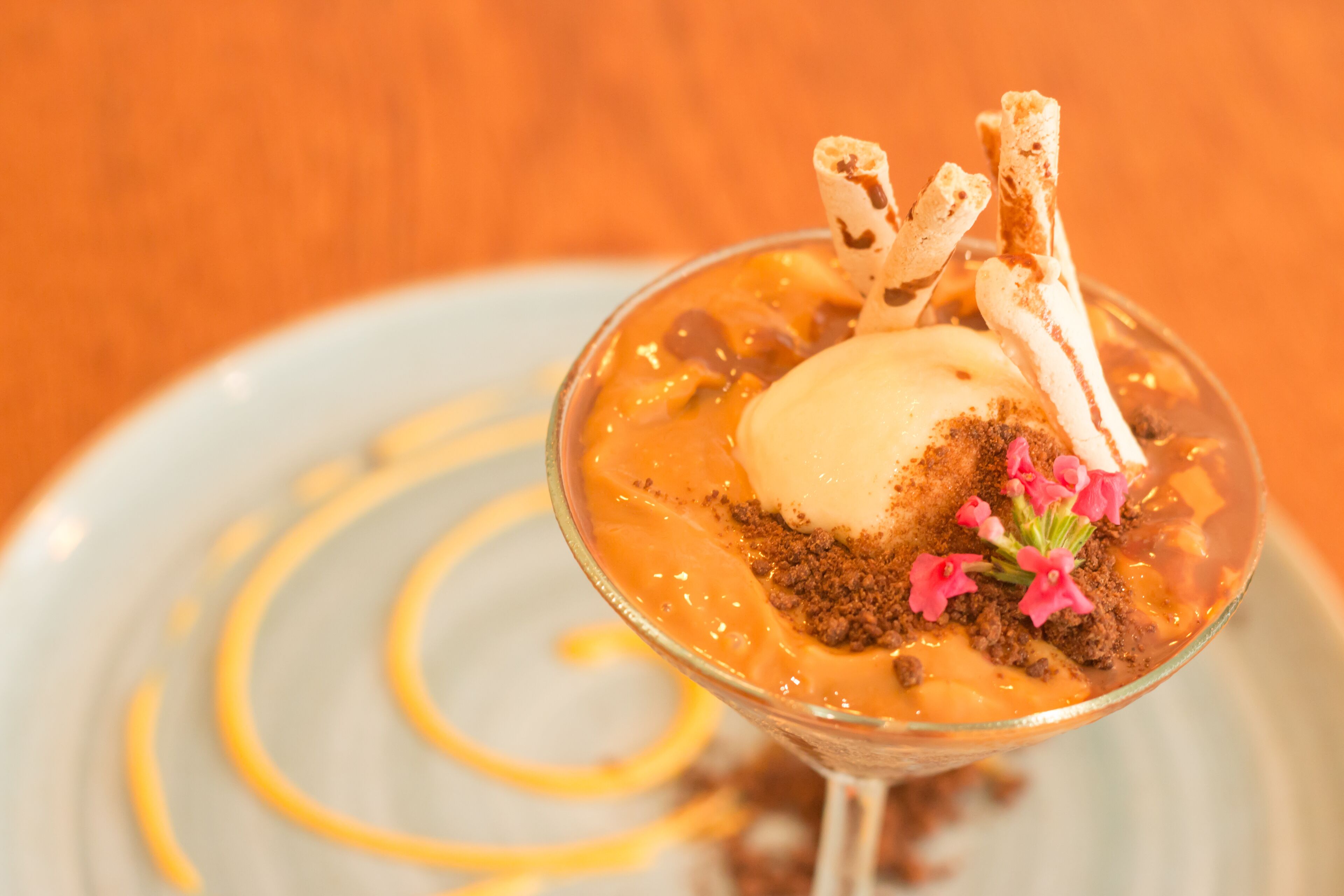 Un dessert servi dans un verre, composé d’une sauce au caramel, d’une boule de glace, de morceaux de chocolat émiettés et d’un décor en chocolat.