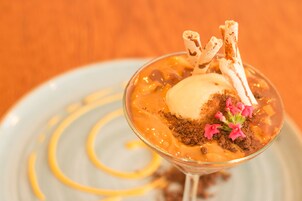 Un dessert servi dans un verre, composé d’une sauce au caramel, d’une boule de glace, de morceaux de chocolat émiettés et d’un décor en chocolat.