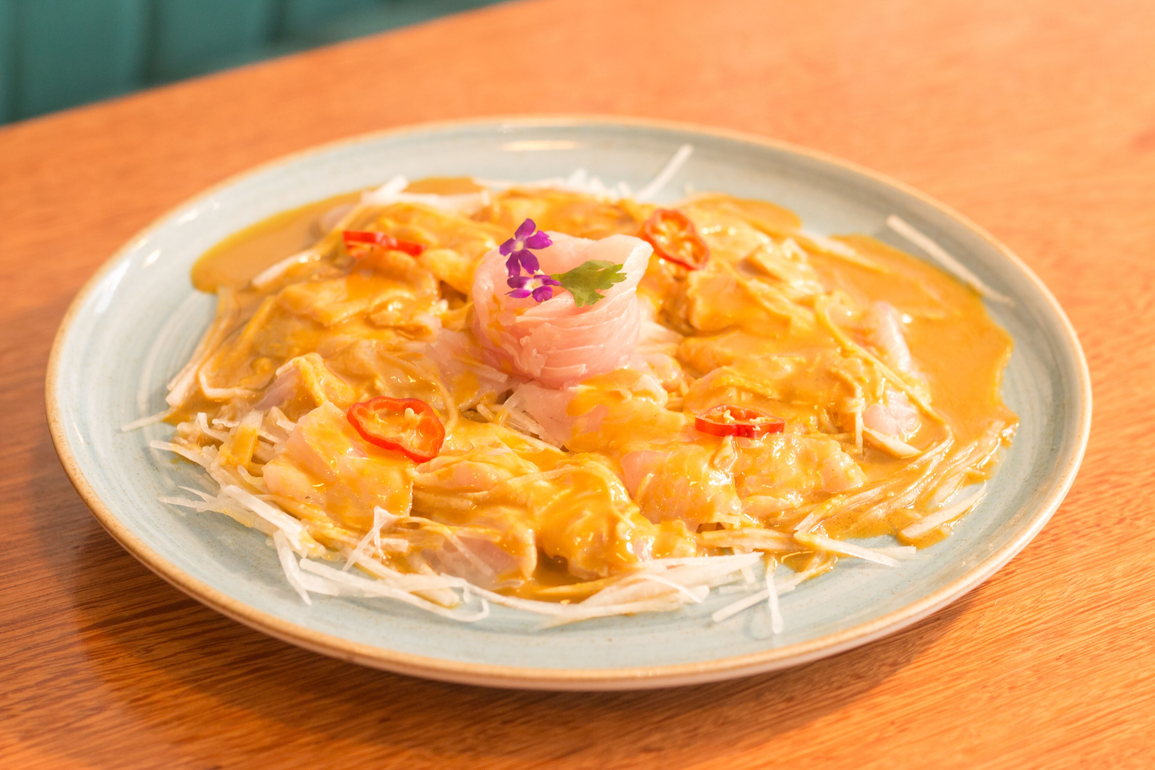 A plate of food with a creamy sauce, sliced red peppers, and a decorative flower on top.
