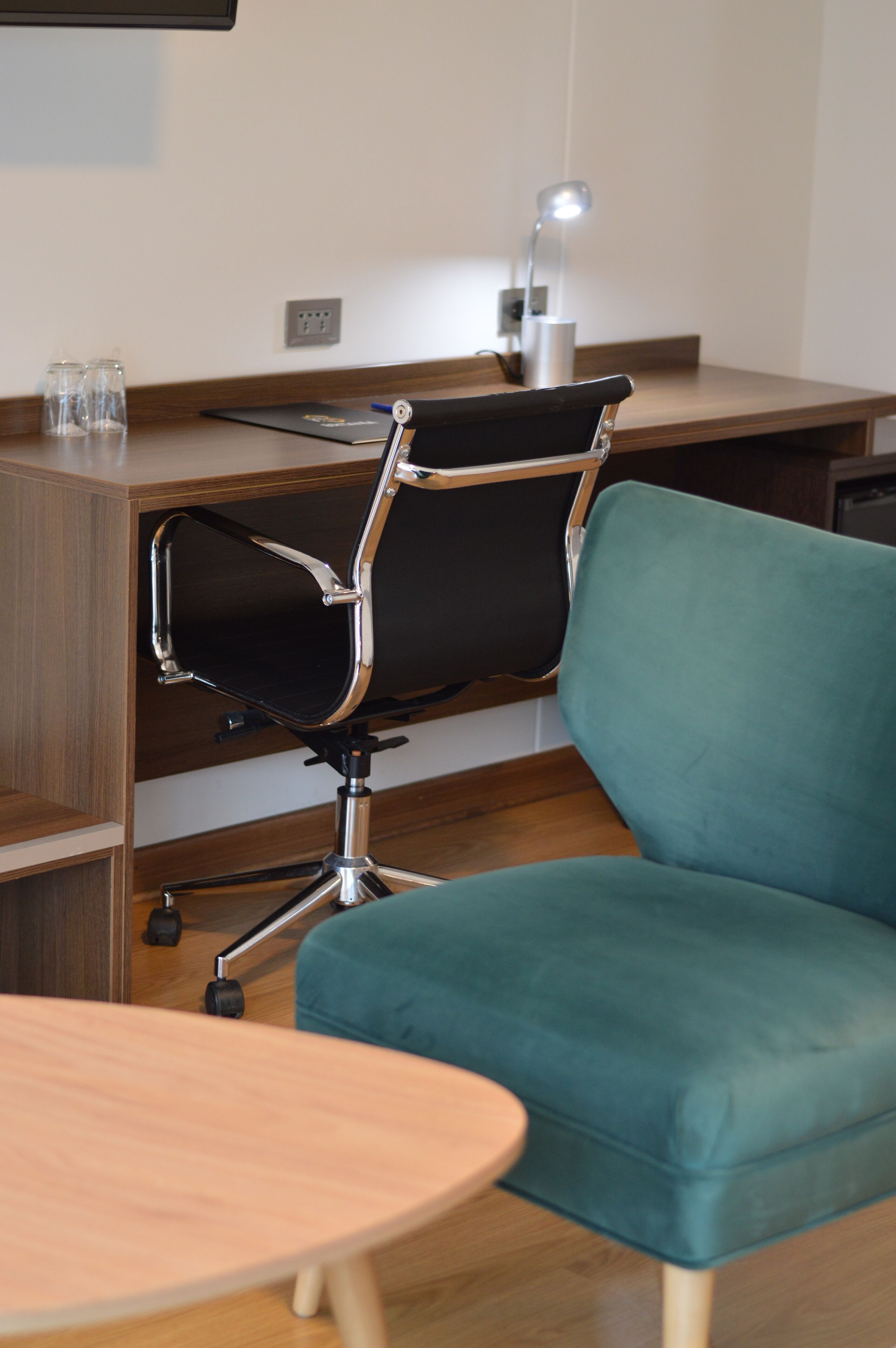 A modern office chair with a black seat and backrest, a teal upholstered armrest, and a chrome base.
