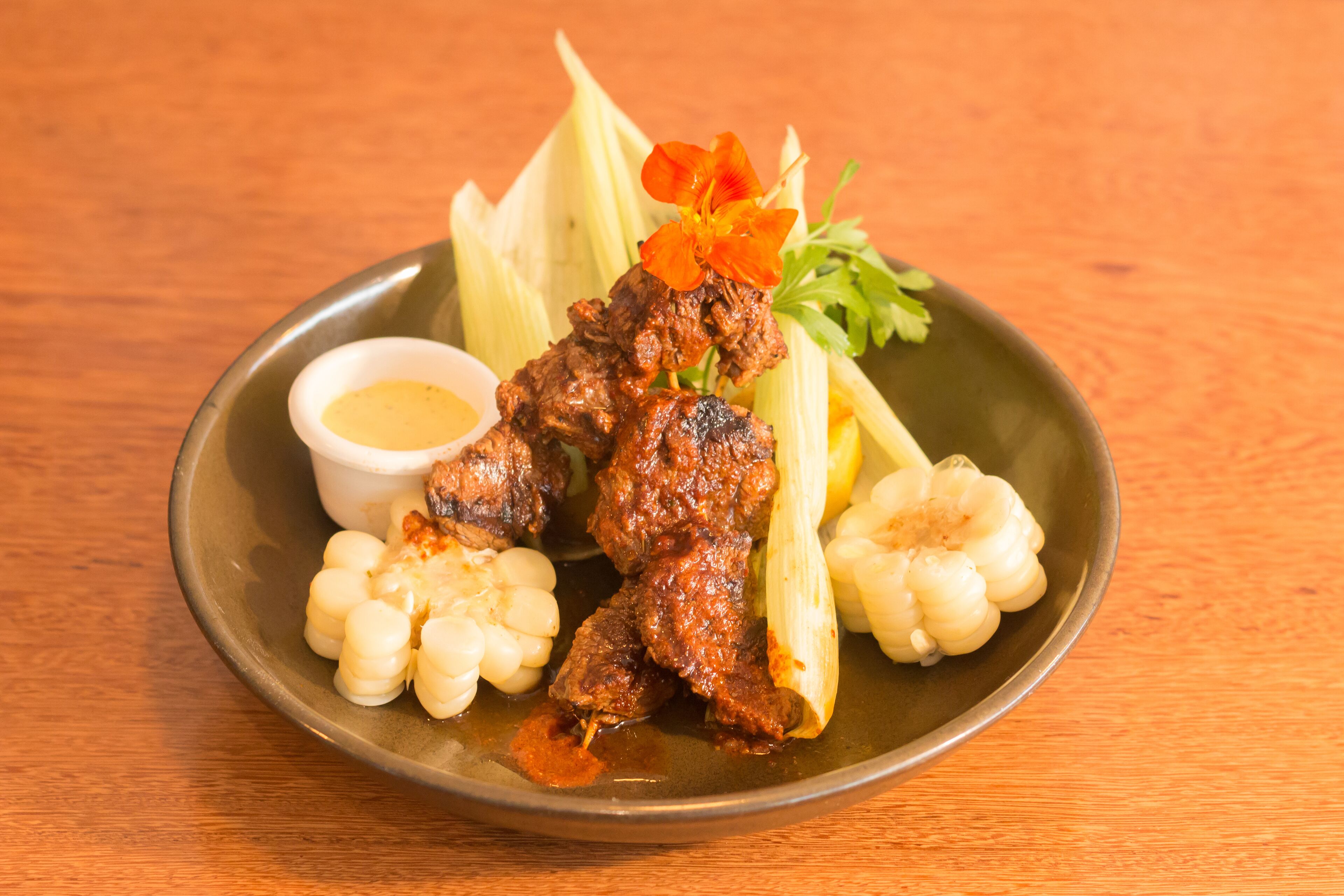 A plate with grilled meat, corn, and a small bowl of sauce.