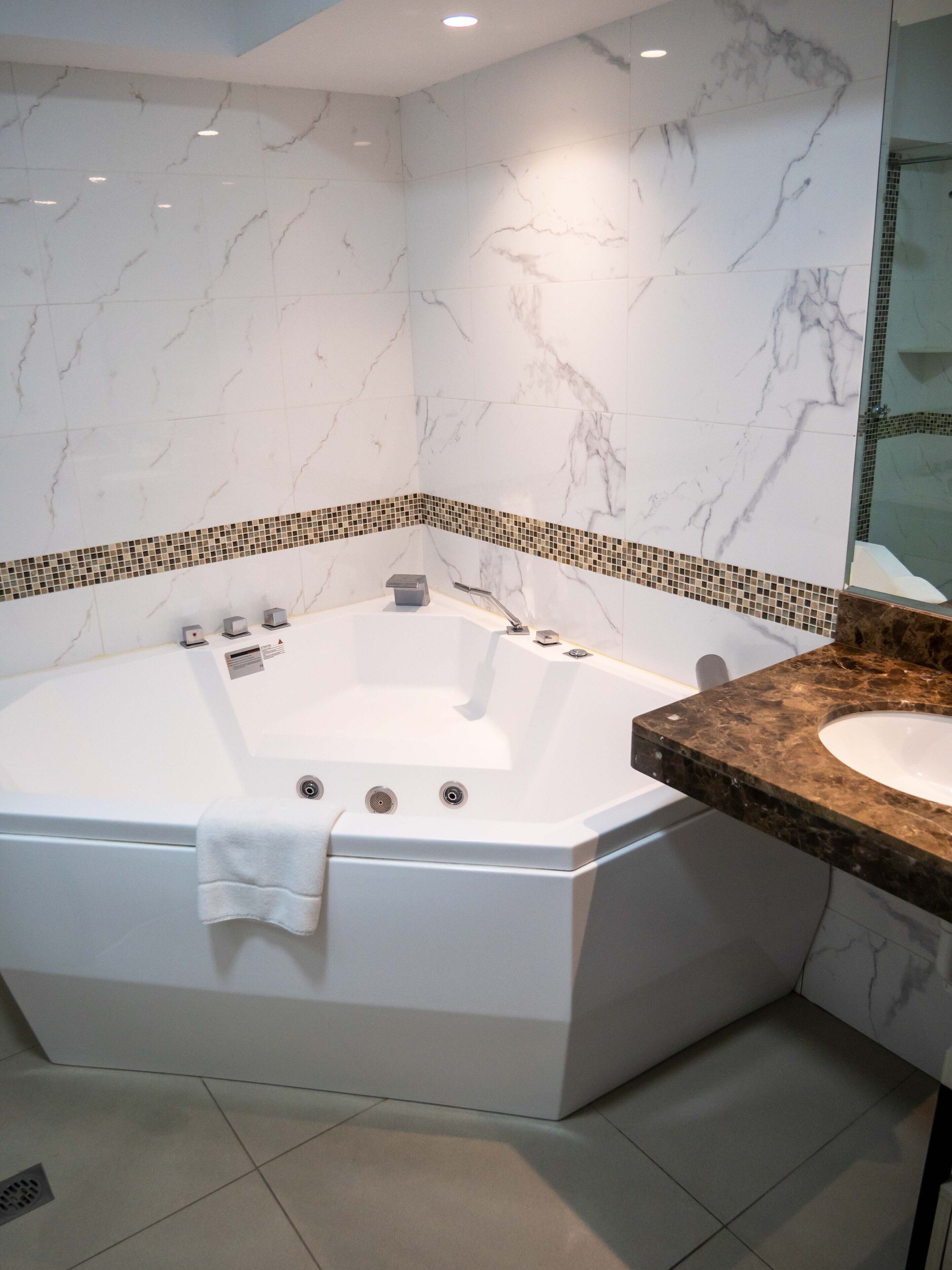 A modern bathroom with a freestanding bathtub, a marble-tiled wall, and a sink with a granite countertop.