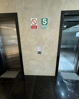 Interior de un ascensor con dos señales: una indica no usar en caso de incendio o humo, y otra marca una zona segura para ascensores.