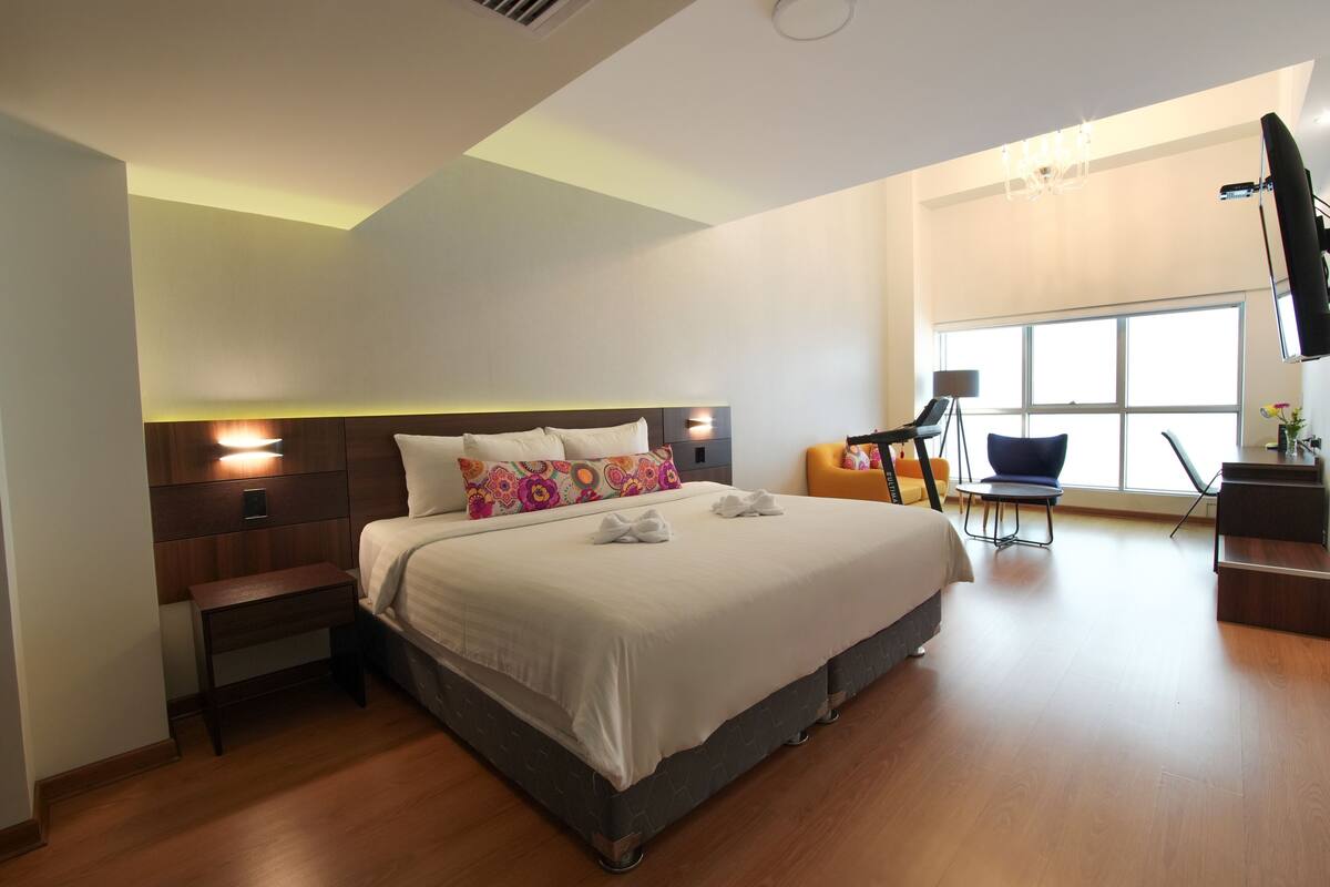 Ein modernes Hotelzimmer mit einem großen Bett, einem Schreibtisch, einem Sessel und einem Fernseher.