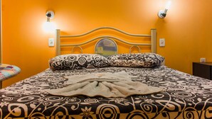 A bed with a patterned bedspread and pillows, a headboard with a light fixture, and a wall socket. - Cavalo Branco Hotel (São Vicente do Sul)