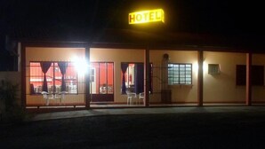 A hotel with a neon sign, a covered entrance, and a visible seating area outside. - Cavalo Branco Hotel (São Vicente do Sul)