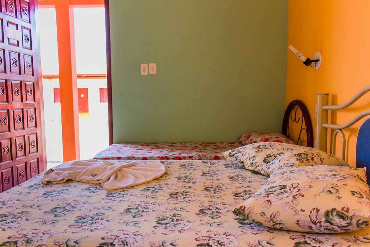 A room with two beds, floral bedding, a wooden door, and a wall-mounted light fixture.