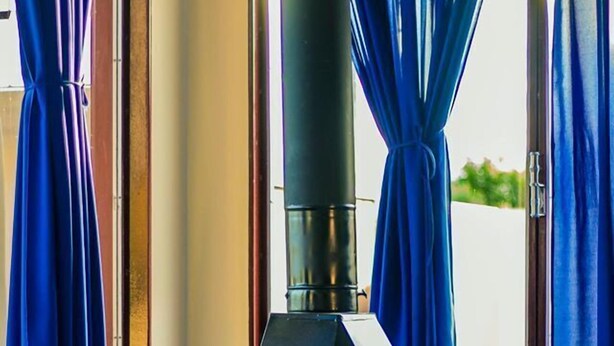 A wood-burning stove in a room with blue curtains and a red chair. - Cavalo Branco Hotel (São Vicente do Sul)