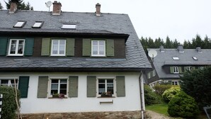 A two-story house with green shutters, a stone foundation, and a sloped roof with satellite dishes. - Cottage on the forest with sauna (Bad Elster)
