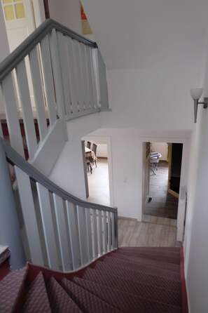 A staircase leading to a second floor with a red carpet. There is a dining area with chairs and a table visible in the background.
