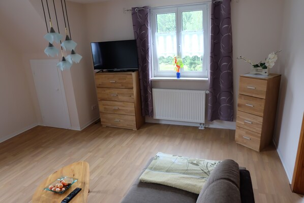 A room with a TV, wooden furniture, a window with curtains, and a small table with a vase. - Cottage on the forest with sauna (Bad Elster)