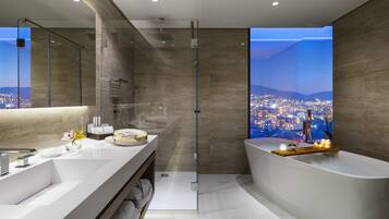 Un baño moderno con una bañera amplia, una ducha con mampara de vidrio y un tocador con vista a la ciudad.