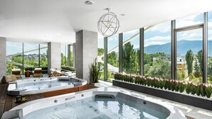 A modern spa area with two hot tubs, wooden flooring, and a view of a cityscape through large windows.