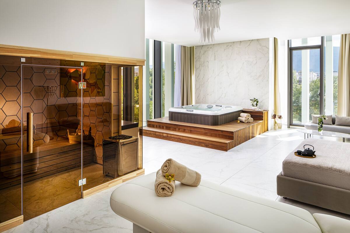 Une salle de spa moderne dotée d’un sauna en verre, d’un bain à remous et d’un espace détente avec des serviettes à disposition.