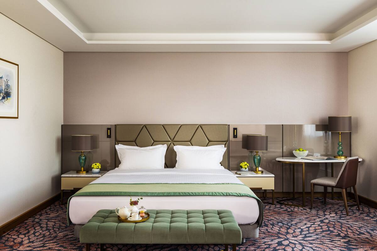 Une chambre d’hôtel avec un grand lit, deux tables de chevet avec des lampes, un petit bureau avec une chaise et une moquette à motifs.