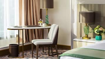 Ein Hotelzimmer mit einem Bett, einem Schreibtisch mit einem Laptop, einem Stuhl, einer Lampe, einer Vase mit Blumen und einem Fenster mit Vorhängen.