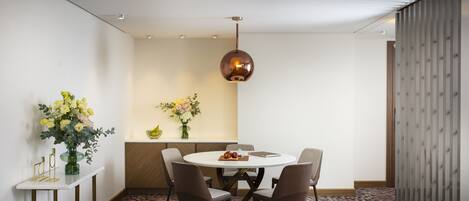 Un comedor con una mesa redonda, cuatro sillas, un florero con flores y una lámpara colgante.