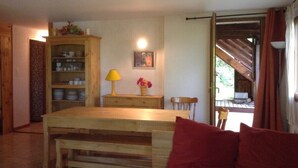 A cozy living room with a wooden dining table, a red sofa, and a cabinet with dishes.