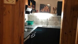 A compact kitchen with wooden walls, a tiled backsplash, and a black countertop.