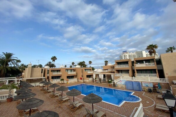 A rooftop pool area with lounge chairs and umbrellas, surrounded by palm trees and a clear sky. - Parque De Las Americas (Adeje)