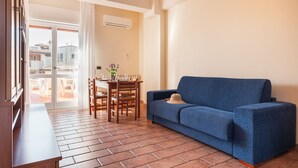 A living room with a blue sofa, a wooden table with chairs, and a view of the outside balcony.