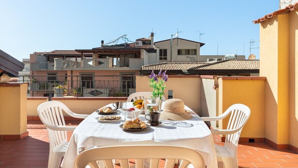 A rooftop terrace with a table set for breakfast, surrounded by white plastic chairs.