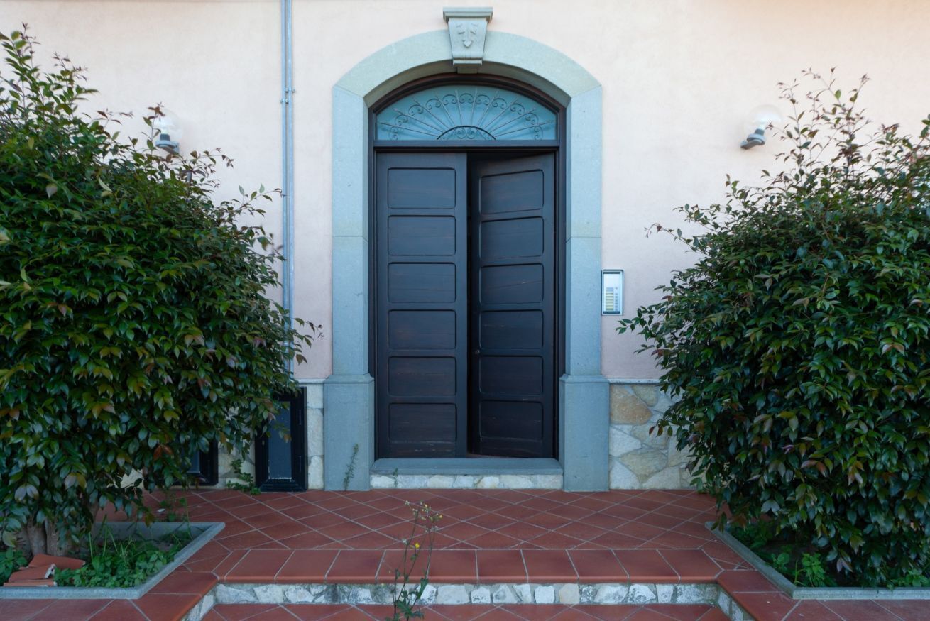 A building entrance with a dark wooden double door, a stone archway, and a tiled pathway leading up to it.