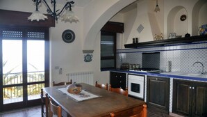 Un'area pranzo con tavolo e sedie in legno, una cucina con piastrelle blu e bianche, e una vista attraverso una porta in vetro.