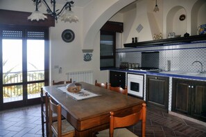 Un comedor con mesa y sillas de madera, una cocina con azulejos azules y blancos, y una vista a través de un ventanal.