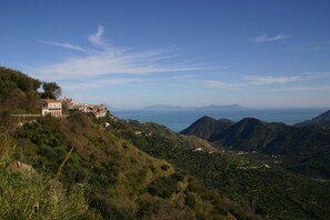 A hillside with a building, possibly a hotel, overlooking a valley and the sea.