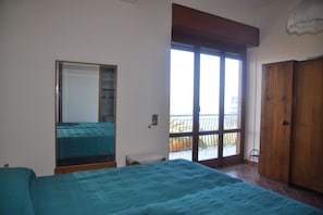 Un dormitorio con cama, armario, ventana y balcón.