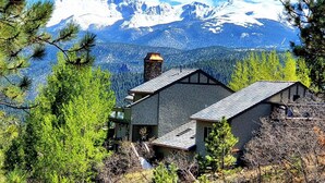 A two-story stone building with a chimney, surrounded by trees and mountains in the background. - Castle with Pikes Peak Views & Hot Tub
Bus. license #008672 (Woodland Park)