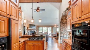 A spacious kitchen with wooden cabinets, a stone accent wall, and a large island with a gas stove. - Castle with Pikes Peak Views & Hot Tub
Bus. license #008672 (Woodland Park)