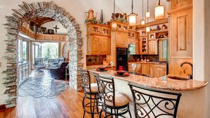 A spacious kitchen with wooden cabinets, a stone archway, and a bar area with stools. - Castle with Pikes Peak Views & Hot Tub
Bus. license #008672 (Woodland Park)