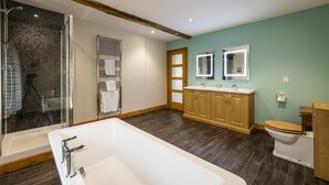 A modern bathroom with a large bathtub, wooden cabinets, a toilet, and a glass shower enclosure. - The Inn at Ravenglass (Ravenglass)