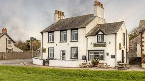 A white building with a pub sign, outdoor seating, and a stone wall in the background. - The Inn at Ravenglass (Ravenglass)