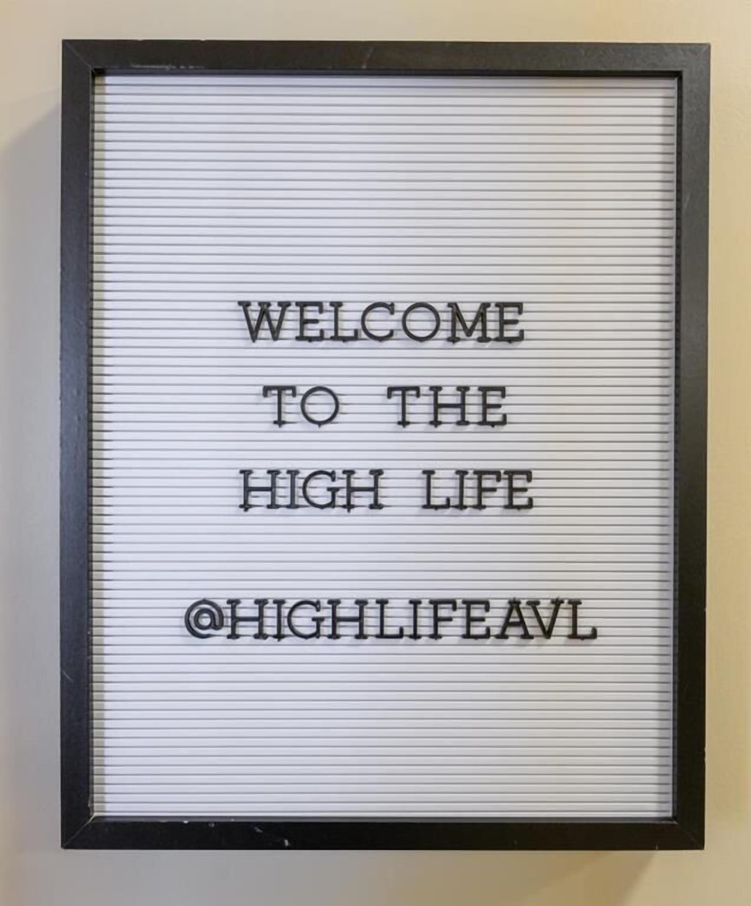 Un letrero en marco con el texto 'WELCOME TO THE HIGH LIFE @HIGHLIFEAVL'.