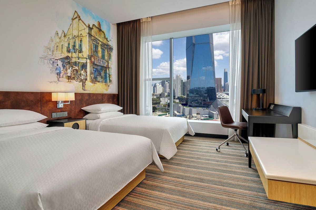 Une chambre d’hôtel avec deux lits, un bureau, une chaise, une télévision et une grande fenêtre donnant sur la ville.